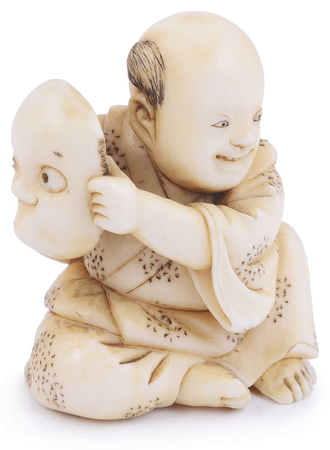 Lot 136 - ~IVORY NETSUKE OF A BOY HOLDING A MASK OF HYOTTOKO