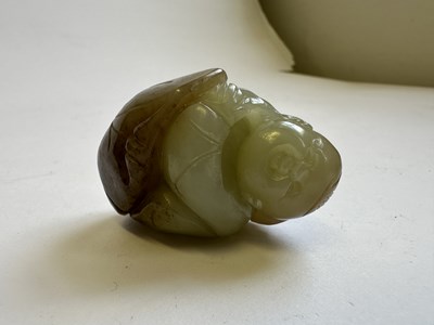 Lot 69 - A CHINESE CELADON AND BROWN JADE CARVING OF A BOY AND LOTUS, QING DYNASTY (1644-1911)